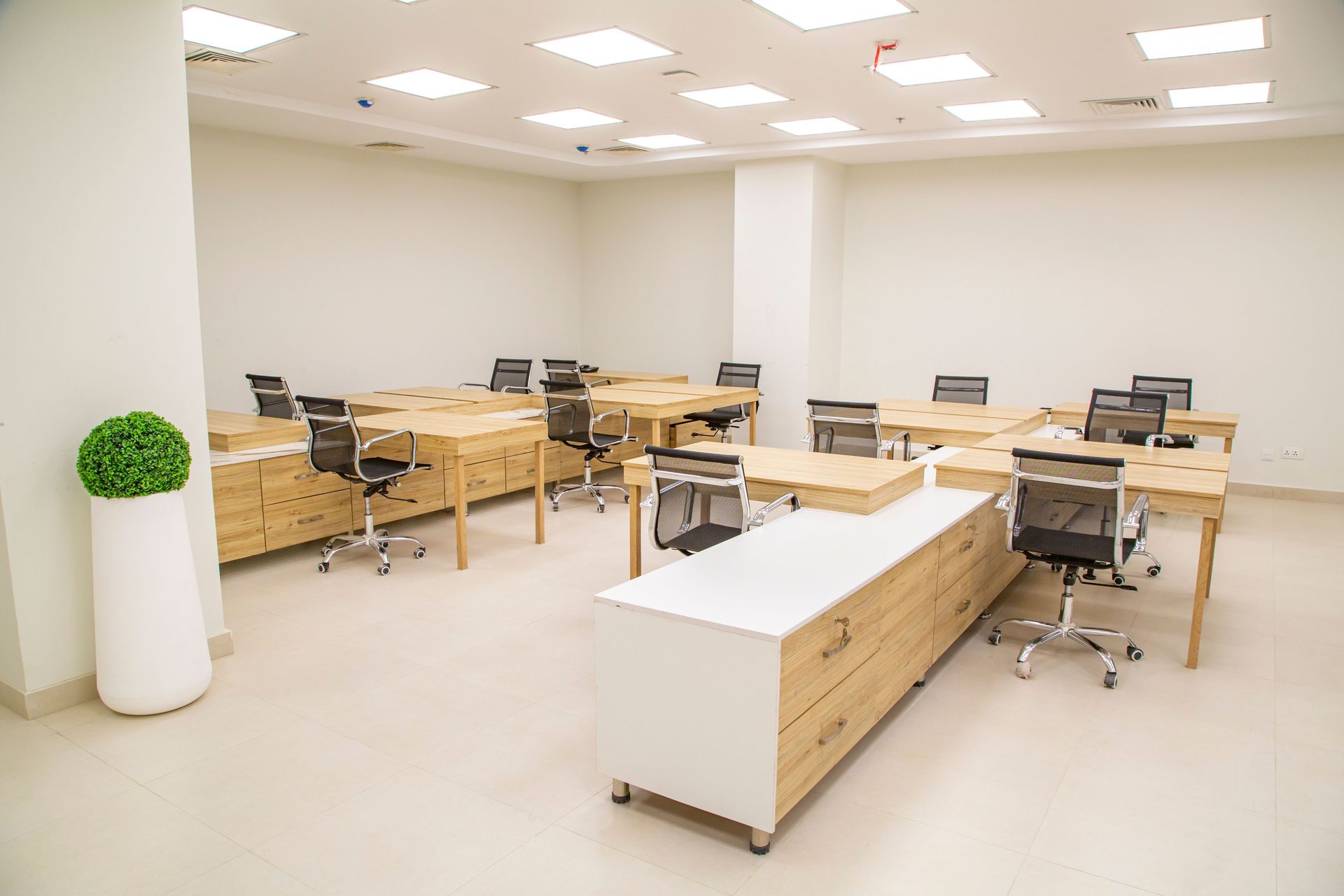 A bright, modern office space featuring wooden desks, rolling chairs, and ample lighting.